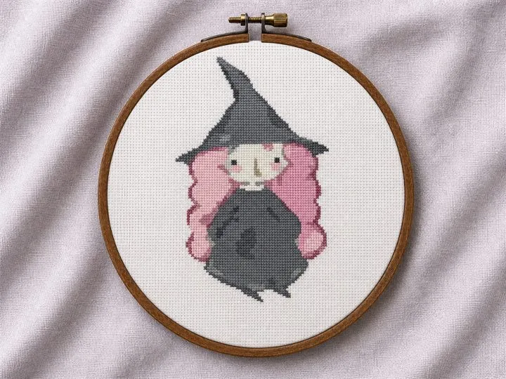 Pink-haired witch cross stitch pattern displayed in a wooden embroidery hoop
