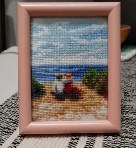 Seaside scene cross stitch in a pink frame, finished by a customer